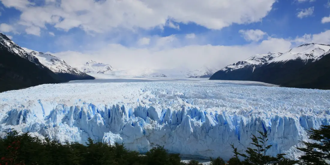 El frente del glaciar Perito Moreno, en la Patagonia argentina, con montañas nevadas y cielo azul