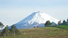 El volcán Cotopaxi nevado sobre los campos verdes de los Andes ecuatorianos