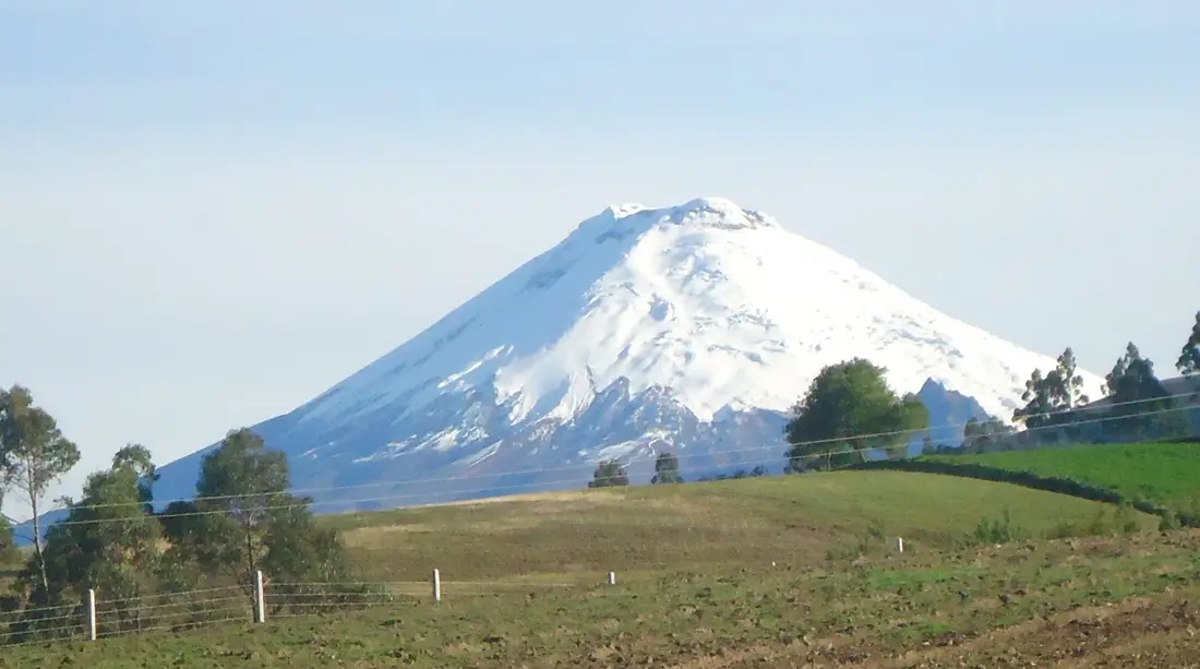El volcán Cotopaxi nevado sobre los campos verdes de los Andes ecuatorianos