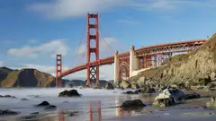 The Golden Gate Bridge in San Francisco seen from Marshall’s Beach, with rocks along the shore and a blue sky