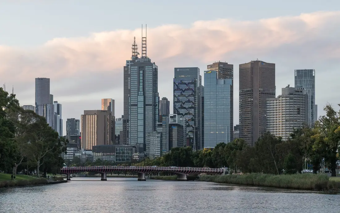Rascacielos del centro de Melbourne sobre el río Yarra, con un puente y árboles en la orilla con luz de última hora de la tarde