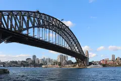 Sydney Harbour Bridge over the harbour, with the North Sydney buildings behind and a blue sky
