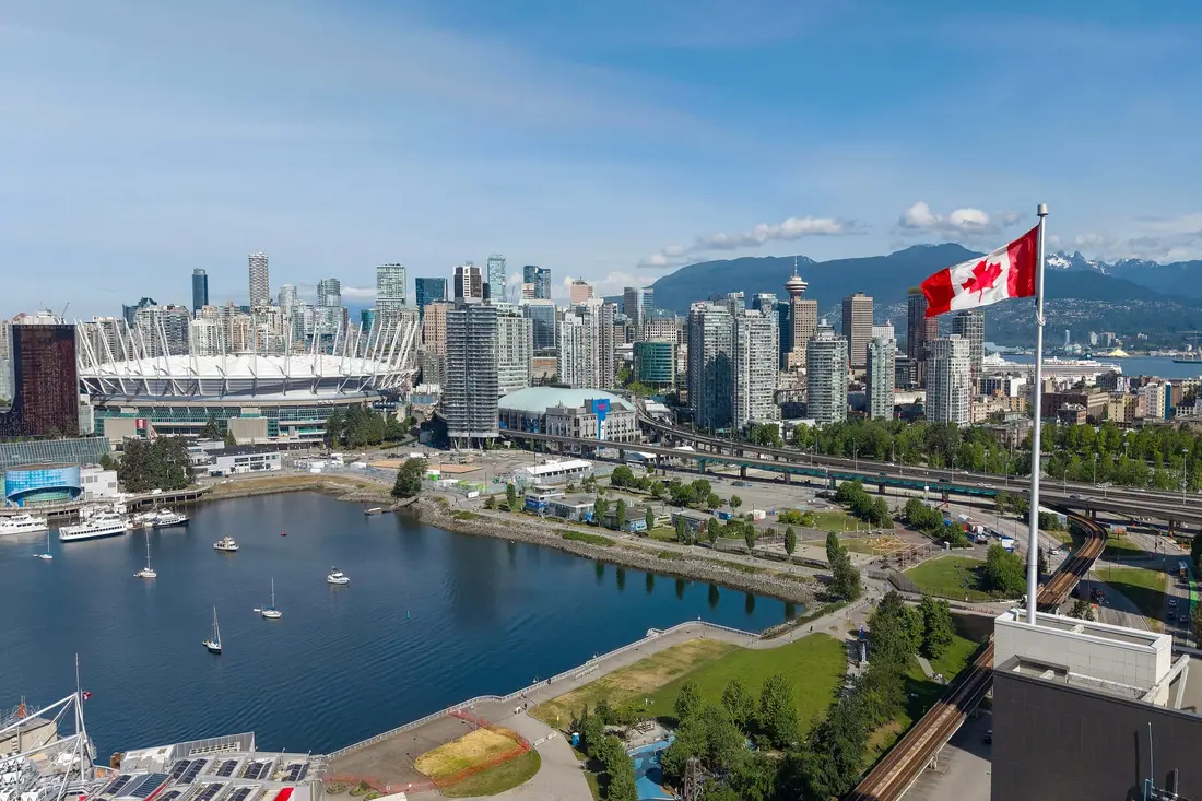 Centro de Vancouver junto a la ensenada de False Creek, con el estadio BC Place, una bandera de Canadá y montañas al fondo
